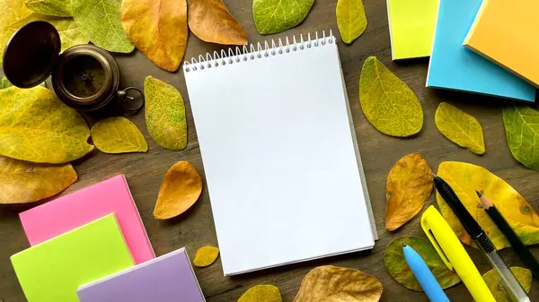 Sonbahar yaprakları ve kırtasiye malzemeleri arasında bir not defteri ve pusula - seyahat, notlar, günlükler ve güzergah planlaması fikri.