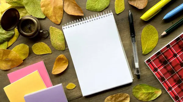 Kırtasiyeli sonbahar kompozisyonu - not defteri, kalem ve defterler sarı ve turuncu yapraklara karşı. Okul konseptine geri dönmek ya da sonbaharda okula gitmek..