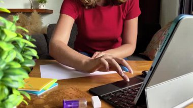 Genç bir kadın tablet üzerinde uzaktan çalışırken yapışkan bir nota not alır. Sahne konsantrasyonu, kendi kendini organize etmeyi ve çalışma sürecine modern bir yaklaşımı sembolize eder..