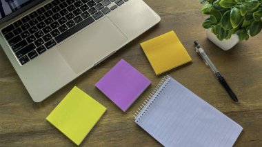 Renkli yapışkan notlar, not defteri, ahşap bir masa üzerinde dizüstü kalem ve dizüstü bilgisayar, projeleri düzenleme ve uzaktan planlama.