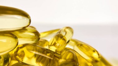 Beyaz arka planda omega-3 balık yağı kapsüllerinin yakın plan çekimi, üst köşesinde yazı için yer var. Parlak altın damlalar sağlıklı takviyelerin değerini ve saflığını gösteriyor..