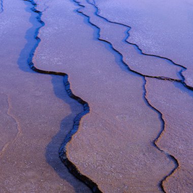 Jeotermal havuz etrafındaki mineral birikintileri tarafından oluşturulan karmaşık desenleri ve dokuları gösteren soyut bir resim, canlı renkler ve ilginç şekiller.