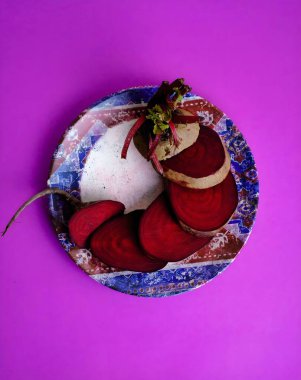 İnce pancar dilimleri, mor bir zemine karşı dekoratif bir plaka üzerinde spiral şeklinde dizilir ve spiral merkezden uzanan yeşil sapları ve yaprakları...