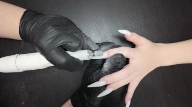 Kısa bir video: Bir tırnak teknisyeninin e-dosya kullanarak ekstra uzun çivi şeklini mükemmelleştirmek için yakın plan çekimi. Kız manikür yaptırıyor. Beyaz tişörtlü kız..
