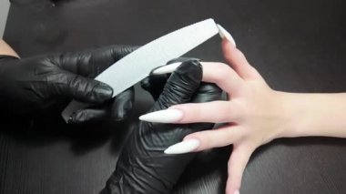 Kısa klip, bir el dosyasıyla uzun sivri uçlu çivilerin son şeklini gösteriyor. Siyah elbiseli, fırçalı kız.