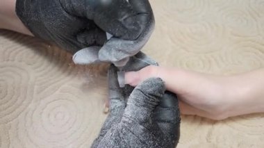 Tırnak teknisyeninin kısa klipsi akrilik çivileri şekle sokuyor, fazlalık ürünü kaldırıyor. Usta güzellik salonunda manikür yapıyor, yakın plan -