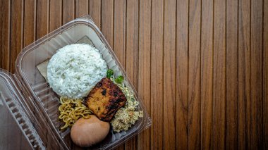 Bancakan, sebze pilavı, rendelenmiş hindistan cevizi (gudangan) ve ahşap arka planda izole edilmiş şeffaf mika kaplarda çeşitli mezeler. Merkez Java halkı için kurtuluş tabağı..