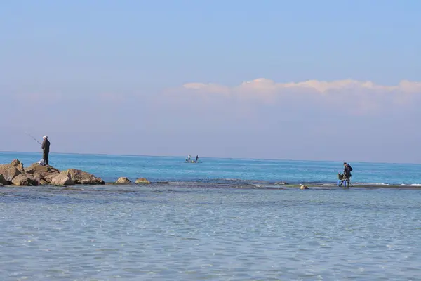 Genç bir adam denizdeki bir kayanın üzerinde duruyor.