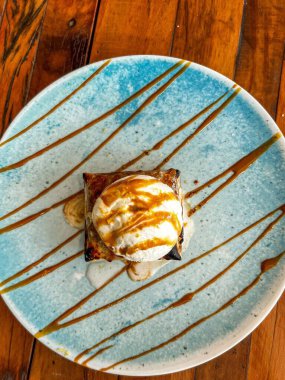 Bir kepçe vanilyalı dondurmayla kaplanmış ve yuvarlak mavi bir tabağın önünde karamel soslu Arjantin usulü bir gözleme içeren gurme tatlısının genel manzarası.