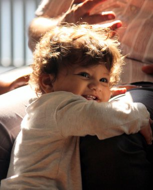 Küçük tatlı çocuk büyükbabasının bacağına sarılıyor. Güneş ışığı saçlarını altın sarısı yapıyor. O çok mutlu bir ruh hali içinde. O, evinde ailesi ile rahatça eğleniyor.. 