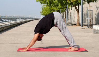Hindistan 'ın Ahmedabad kentindeki Riverfront' ta kıdemli bir adam, Adho Mukha Svanasana pozunda yoga yapıyor. 60 'lı yaşlarının başında açık hava sağlığını ve sağlıklı bir yaşam tarzını kucaklıyor.. 