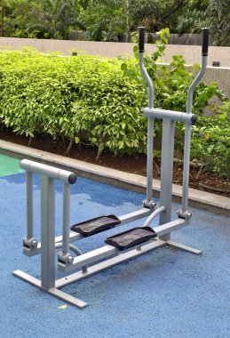 Açık hava eliptik eğitmeni yeşil bir park ortamında canlı mavi bir paspas üzerinde, temiz hava ve doğal çevreye sahip toplumsal fitness ve kardiyovasküler sağlık için tasarlanmıştır..