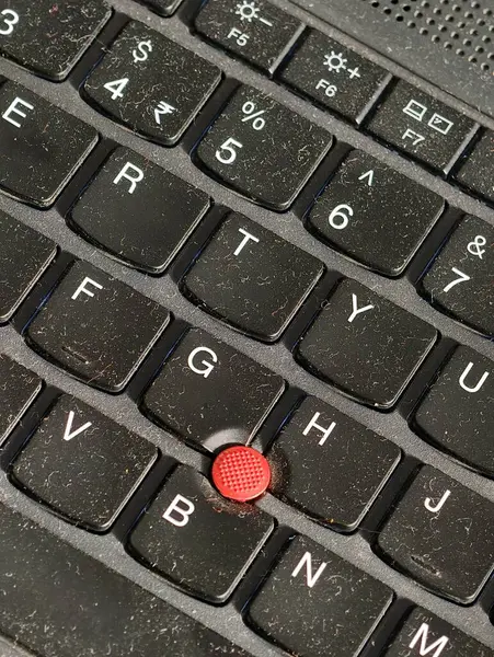İmleç denetimi için kullanılan kırmızı TrackPoint çıkıntılı bir dizüstü bilgisayarın klavyesine yakın plan, modern çalışma alanındaki tozlu tuş gösterici klasik teknoloji tasarımı ile çevrili.