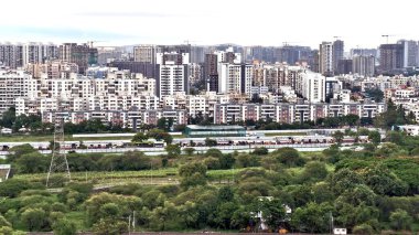 Yoğun kentsel konutların panoramik görüntüsü ve inşaat vinçleri ve yeşil alanlardan oluşan yüksek binalar, hızlı şehir gelişiminin özünü yakalıyor. 15 Haziran 2025, Pune Hindistan