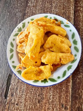 Süslü bir tabakta kızartılmış altın sarısı muzlar, kırsal ahşap bir yüzeye yerleştirilmiş, geleneksel yemek kavramlarını ve lezzetli tatlıları resmetmek için ideal..