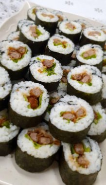 Deniz yosunu ve beyaz pirince sarılı çeşitli malzemelerden oluşan taze hazırlanmış suşi tabağı, canlı yeşil sebzeler ve lezzetli domuz parçaları..