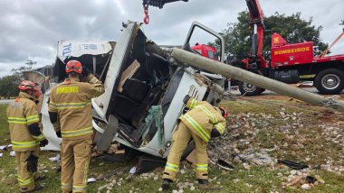 İtfaiyecilerin kamyon kazasından sonraki görüntüsü. Profesyoneller kargoyu geri almak için çalışıyorlar, kamyonun parçaları devrildi ve yakınlarda bir vinç var. Sahne aciliyet ve dayanışmayı ifade ediyor.