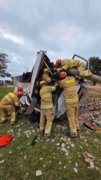 İtfaiyeciler görev başında, devrilmiş bir kamyonu dramatik bir şekilde kurtarıyorlar. Olay yerinde, kurtarma ekipleri acil bir durumda kurbanlara yardım etmek için ekipman kullanırken cesaret ve takım çalışması vurgulanıyor. Bulutlu gökyüzü aciliyet katıyor.