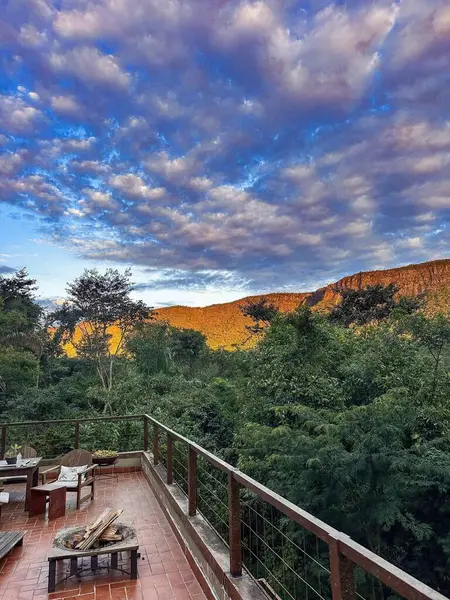 Balkondan çekilen çarpıcı bir sahne dramatik bulutlardan yansıyan ateşli turuncu günbatımı renkleriyle dağların panoramik manzarasını gösteriyor. Yeşillik
