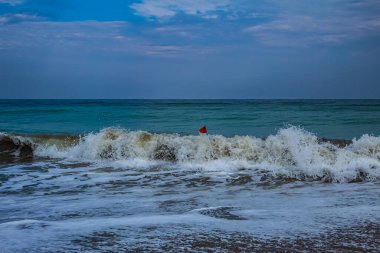 Siyah bir arka planda dalgayla deniz kıyısında yürüyen bir adamın dikey görüntüsü.