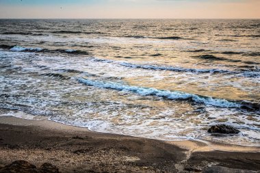 Deniz kıyısında bir dalgayla gün batımı