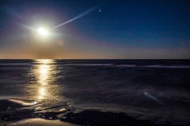 Donmuş bir göl manzarası. Ufukta dolunay var. Gece gökyüzünde.