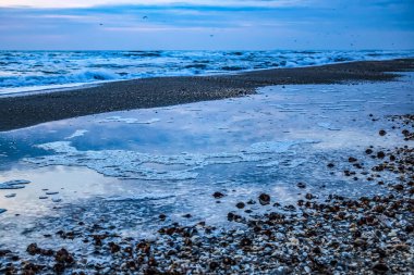 Kışın gün batımında buzlu ve taşlı deniz kıyısı.
