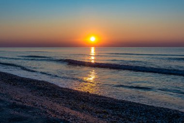 Sahilde gün doğumu ön planda küçük bir dalgayla