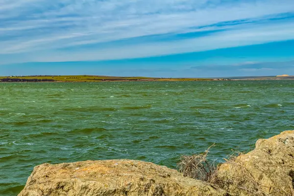 Bulutlu bir gökyüzünün altında kayalık bir sahille çevrili büyük beyaz bir göl.