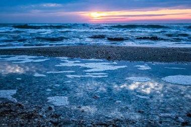 Deniz kıyısında gün batımı, dalgalar ve bulutlar