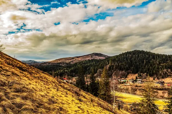 Bulutlu gökyüzünün altında yeşilliklerle çevrili güzel bir dağ manzarası.