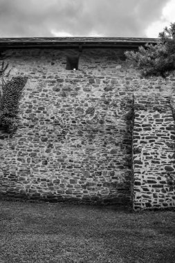 Bulutlu bir gökyüzünün altında yeşillikle çevrili bir taş evin dikey görüntüsü.