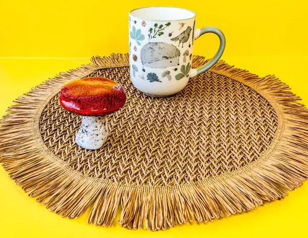 Bir fincan kahve, bir fincan çay, sarı arka planda bir hasır şapka.