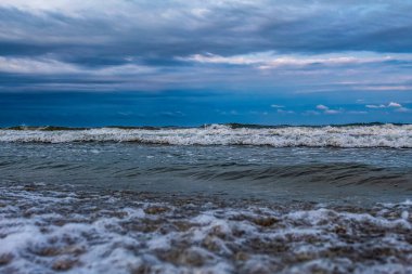 Deniz dalgaları ve köpükler gün batımında sahilde