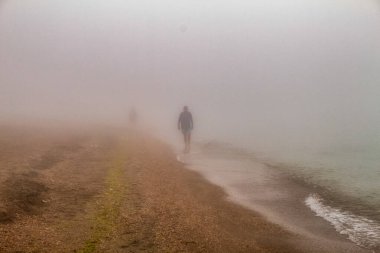 Sahilde yürüyen beyaz ceketli bir adam.