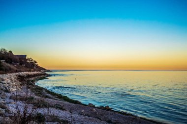 Akdeniz kıyısında gün batımı ön planda kayalarla.