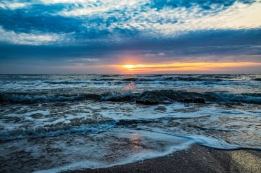 Dalgalar ve güzel bulutlarla denizin üzerinde gün batımı