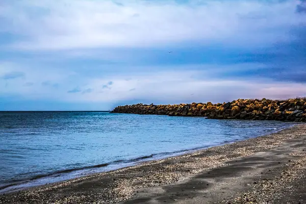 Gökyüzünde bulutlar olan deniz ve kayalar.