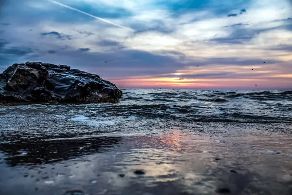 Sahilde gün batımı ve arka planda bir dalga.