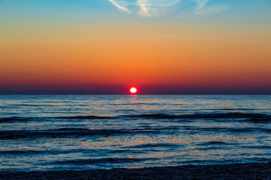 Güneş ufuktaki bulutların arasından parlıyor.