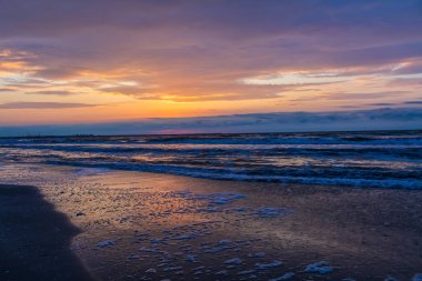 Bulutlar ve dalgalarla denizin üzerinde gün batımı.