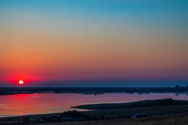 Yaz akşamında gün batımı, güneş suya yansıyor.