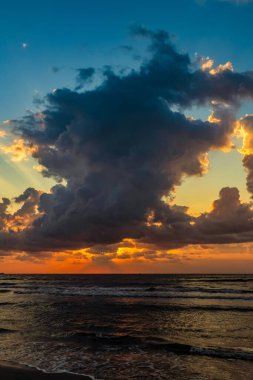 Deniz sahilinde gün batımı güzel bulutlu bir gökyüzünde, arka planda, güneş bulutların üzerinde parlıyor, akşamları.