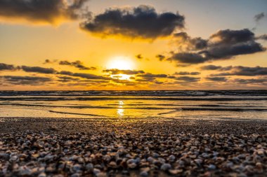 Denizde gün batımı, dalgalı kumsal, güneş, ufuk ve bulutlu güzel bir gökyüzü.
