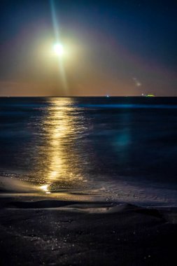 Geceleyin dolunay ve üzerinde küçük bir dalga..