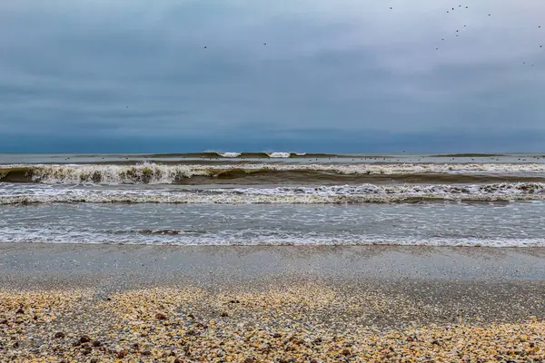 Denizde fırtına bulutları ve dalgalar ön plandaki kayalara çarpıyor.