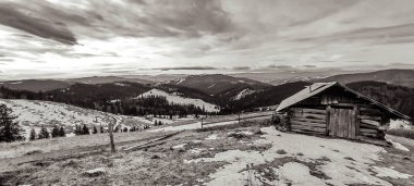 Bulutlu gökyüzünün altındaki dağlarda tahta bir evin dikey görüntüsü.