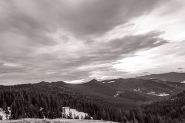 Arkasında dağlar ve ormanlar olan siyah ve beyaz bir manzara.