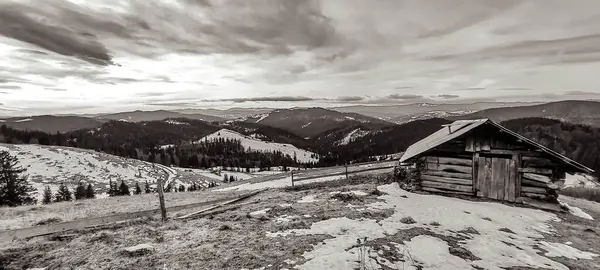 Bulutlu gökyüzünün altındaki dağlarda tahta bir evin dikey görüntüsü.