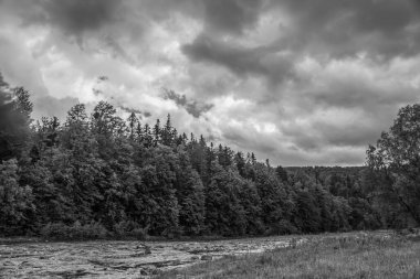 Nehir üzerinde kara fırtına bulutları, yağmurda yeşil orman